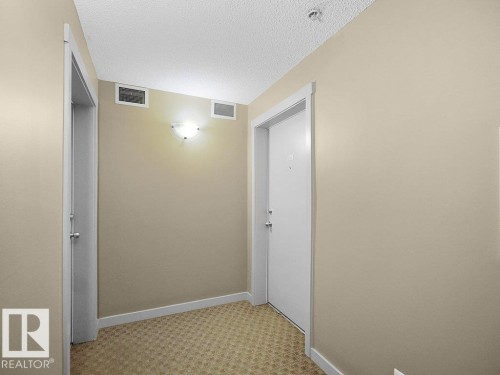 Entryway featuring neutral-toned walls, patterned carpeting, white baseboards, and a contemporary wall sconce - 216 5390 Chappelle Road, Edmonton, AB - Indoor Photo Showing Other Room