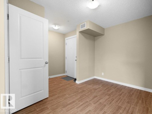 Open interior space featuring wood-finish tile flooring and neutral wall tones - 216 5390 Chappelle Road, Edmonton, AB - Indoor Photo Showing Other Room