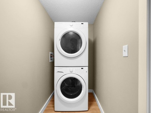Dedicated laundry area featuring a stacked washer and dryer unit, wood-finish flooring, and light-toned wall paint with white trim - 216 5390 Chappelle Road, Edmonton, AB - Indoor Photo Showing Laundry Room