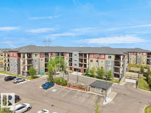 Multi-story residential building featuring a stone and siding exterior, private balconies, surface parking, and a detached security or utility building - 216 5390 Chappelle Road, Edmonton, AB - Outdoor With Balcony