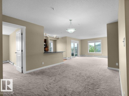 Spacious living area featuring neutral carpeting, a contemporary ceiling light fixture, and a sliding glass door to an outdoor space - 216 5390 Chappelle Road, Edmonton, AB - Indoor Photo Showing Other Room