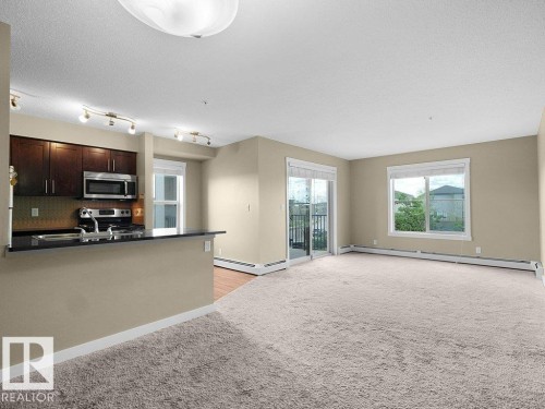 Open-concept living space with light-toned carpeting and neutral wall paint - 216 5390 Chappelle Road, Edmonton, AB - Indoor Photo Showing Kitchen