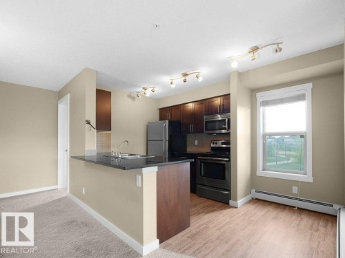 Kitchen area featuring dark wood-finish cabinetry, stainless steel appliances, a black countertop, and a double-basin sink - 216 5390 Chappelle Road, Edmonton, AB - Indoor Photo Showing Kitchen With Stainless Steel Kitchen
