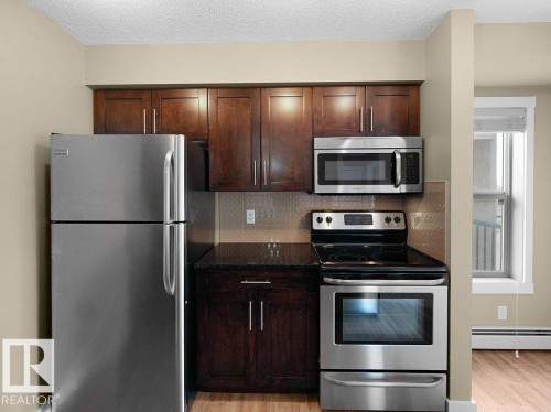 Kitchen featuring stainless steel appliances, dark wood-finish cabinetry, and a textured backsplash - 216 5390 Chappelle Road, Edmonton, AB - Indoor Photo Showing Kitchen With Stainless Steel Kitchen