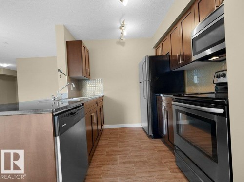 Kitchen featuring wood-finish flooring, dark stone-finish countertops, stainless steel appliances, and a mosaic tile backsplash - 216 5390 Chappelle Road, Edmonton, AB - Indoor Photo Showing Kitchen With Stainless Steel Kitchen