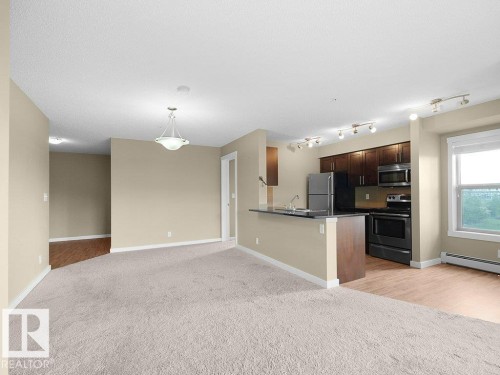 Open-concept living space featuring light neutral wall tones, textured carpeting, and wood-finish flooring - 216 5390 Chappelle Road, Edmonton, AB - Indoor Photo Showing Kitchen