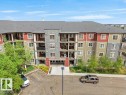 Multi-story residential building featuring a gabled roofline, stone veneer accents, individual balconies, ground-level parking, and mature landscaping - 216 5390 Chappelle Road, Edmonton, AB  - Outdoor With Balcony With Facade 