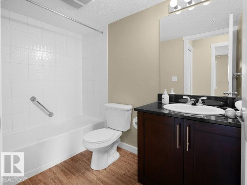 Bathroom featuring a white bathtub, toilet, and a dark wood-finish vanity with a dark countertop and undermount sink - 216 5390 Chappelle Road, Edmonton, AB - Indoor Photo Showing Bathroom