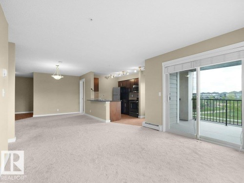 Open-concept living space featuring light-toned carpet flooring and a sliding glass door leading to a private balcony - 216 5390 Chappelle Road, Edmonton, AB - Indoor