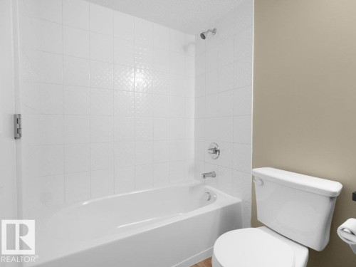 Bathroom featuring a white bathtub with a tiled surround, chrome fixtures, and a white toilet - 216 5390 Chappelle Road, Edmonton, AB - Indoor Photo Showing Bathroom