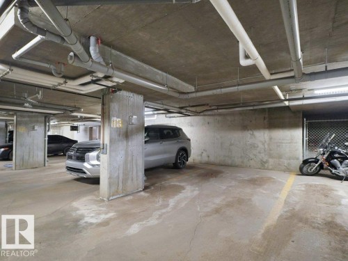 Underground parking space featuring concrete walls, concrete flooring, overhead piping, and fluorescent lighting - 216 5390 Chappelle Road, Edmonton, AB - Indoor Photo Showing Garage