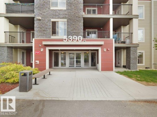 Building entrance featuring multi-toned siding, stone accents, and glass doors - 216 5390 Chappelle Road, Edmonton, AB - Outdoor With Balcony