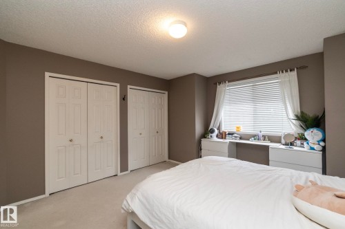 Neutral-toned room featuring a large window with white blinds, two sets of bi-fold closet doors, and plush carpet flooring - 9112 166 Avenue, Edmonton, AB - Indoor Photo Showing Bedroom