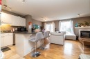 Open-concept living space featuring a kitchen with white cabinetry and a breakfast bar, wood-finish flooring, a fireplace with a tile surround, and large windows - 9112 166 Avenue, Edmonton, AB  - Indoor With Fireplace 