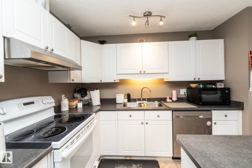 Kitchen featuring white cabinetry, dark countertops, a stainless steel dishwasher, a stainless steel range hood, and a dual-basin stainless steel sink - 9112 166 Avenue, Edmonton, AB - Indoor Photo Showing Kitchen With Double Sink