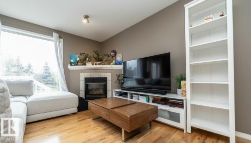 Living area with wood-finish flooring, large picture window, and a built-in fireplace featuring a tile surround and mantel - 9112 166 Avenue, Edmonton, AB - Indoor Photo Showing Living Room With Fireplace