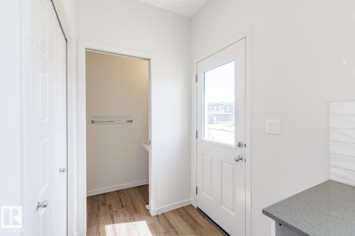 Entry area featuring light wood-finish flooring, a white paneled door with a glass insert, and a built-in countertop with a textured tile backsplash - 3613 Triomphe Boulevard N, Beaumont, AB - Indoor Photo Showing Other Room