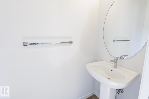 Pedestal sink with chrome faucet, complemented by a large oval mirror and chrome towel bar - 3613 Triomphe Boulevard N, Beaumont, AB - Indoor Photo Showing Bathroom