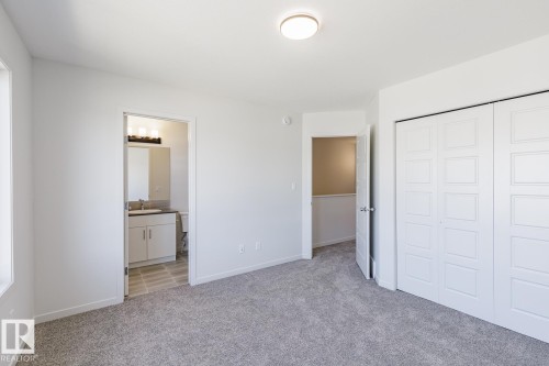 Carpeted room featuring a ceiling-mounted light fixture, white bi-fold closet doors, and access to a bathroom with a vanity and mirror - 3613 Triomphe Boulevard N, Beaumont, AB - Indoor