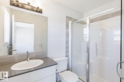 Contemporary bathroom featuring a spacious glass-enclosed shower, single vanity with a gray stone countertop, and a large wall-mounted mirror - 