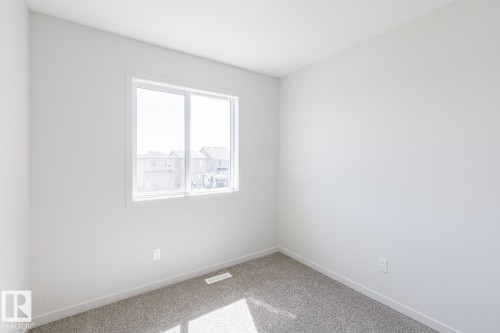 Bright room featuring a large white-framed window, neutral gray carpet, white baseboards, and light-toned walls - 3613 Triomphe Boulevard N, Beaumont, AB - Indoor Photo Showing Other Room