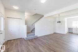 Open concept living space featuring wood-finish flooring, a carpeted staircase, and contemporary lighting fixtures - 