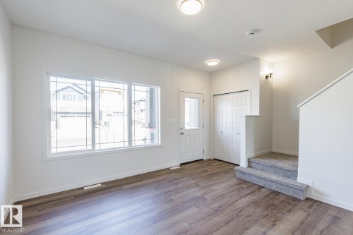 Bright living space featuring wood-finish flooring, a large multi-pane window, a white entry door with glass insert, bi-fold closet doors, and carpeted stairs - 3613 Triomphe Boulevard N, Beaumont, AB - Indoor Photo Showing Other Room