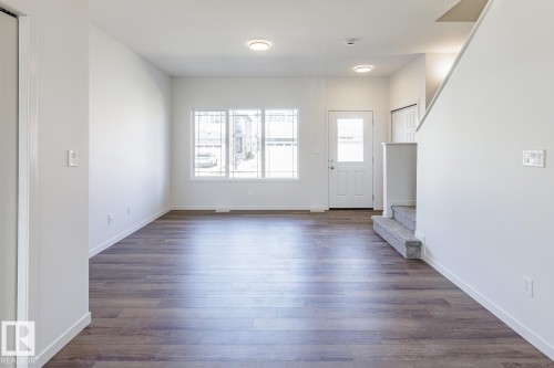 Spacious living area featuring wood-finish flooring, ample natural light from multiple windows, recessed ceiling lighting, a white entry door with frosted glass, and a carpeted staircase with a white railing - 3613 Triomphe Boulevard N, Beaumont, AB - Indoor Photo Showing Other Room