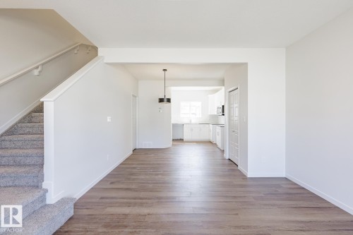 Open-concept living area featuring wood-finish flooring, a carpeted staircase with white railing, and a modern pendant light fixture - 3613 Triomphe Boulevard N, Beaumont, AB - Indoor Photo Showing Other Room