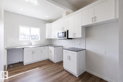 Modern kitchen featuring white cabinetry, dark countertops, a white subway tile backsplash, wood-finish flooring, and recessed lighting - 3613 Triomphe Boulevard N, Beaumont, AB - Indoor Photo Showing Kitchen
