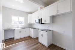 Modern kitchen featuring white cabinetry, dark countertops, a white subway tile backsplash, wood-finish flooring, and recessed lighting - 