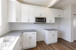 Kitchen featuring white cabinetry with brushed nickel hardware, a stainless steel microwave, gray countertops, a subway tile backsplash, and wood-finish flooring - 