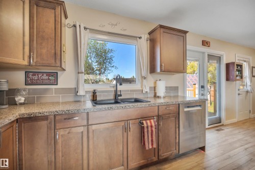 Kitchen workspace featuring a double basin sink with a black faucet, granite-patterned countertops, and light wood-finish cabinetry - 112 Oak Drive, Wetaskiwin, AB - Indoor Photo Showing Kitchen With Double Sink