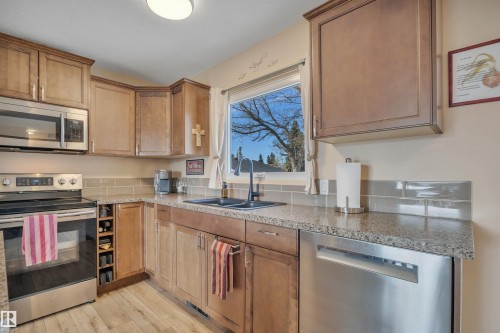 Kitchen featuring stainless steel appliances, wood-finish cabinetry, granite-style countertops, a light gray subway tile backsplash, and wood-finish flooring - 112 Oak Drive, Wetaskiwin, AB - Indoor Photo Showing Kitchen With Double Sink