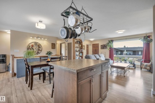 Open-concept living space featuring wood-finish flooring, a kitchen island with stone-look countertop, a dining area, and a living area with a large window - 112 Oak Drive, Wetaskiwin, AB - Indoor Photo Showing Dining Room