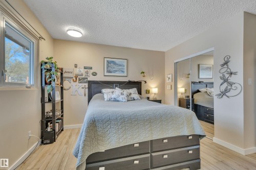 Bedroom featuring wood-finish flooring, a window with natural light, mirrored closet doors, a built-in bed frame with storage drawers, and a ceiling-mounted light fixture - 112 Oak Drive, Wetaskiwin, AB - Indoor Photo Showing Bedroom