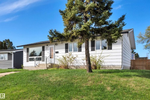 White siding exterior with black window shutters and a mature evergreen tree - 112 Oak Drive, Wetaskiwin, AB - Outdoor