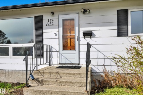 White horizontal siding exterior with a wood-panel front door - 112 Oak Drive, Wetaskiwin, AB - Outdoor With Exterior