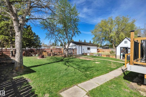 Expansive backyard featuring a lush lawn, mature trees, concrete pathway, rear detached garage, and an additional storage shed - 112 Oak Drive, Wetaskiwin, AB - Outdoor