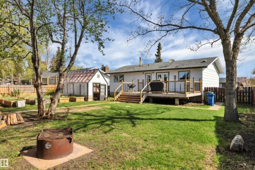 Expansive backyard featuring a large elevated wood deck with railing, a detached greenhouse, multiple raised garden beds, and a fire pit area - 112 Oak Drive, Wetaskiwin, AB - Outdoor With Deck Patio Veranda