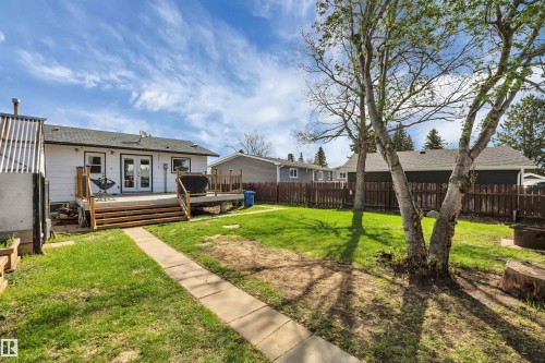 Spacious backyard featuring a wooden deck with railing, lawn space, and mature trees - 112 Oak Drive, Wetaskiwin, AB - Outdoor With Deck Patio Veranda