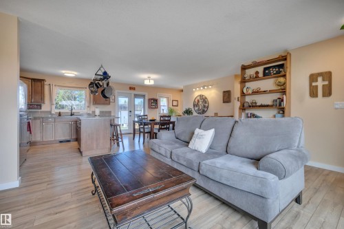 Open-concept living area featuring wood-finish flooring, a kitchen island with seating, dark wood cabinetry, a built-in shelving unit, and a dining area with direct outdoor access - 112 Oak Drive, Wetaskiwin, AB - Indoor Photo Showing Living Room