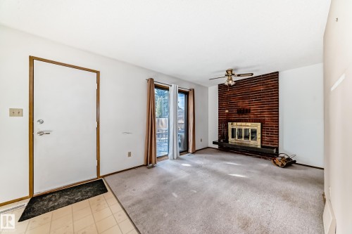Living area featuring a brick-surround fireplace with a brass firebox, a ceiling fan, sliding glass doors, and carpet flooring - 9528 189 Street, Edmonton, AB - Indoor With Fireplace