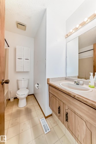 Bathroom featuring a wood-finish vanity with an integrated sink, a wall-mounted mirror, and a vanity light fixture - 9528 189 Street, Edmonton, AB - Indoor Photo Showing Bathroom
