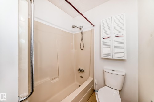 Bathroom featuring a shower/tub combination with a curved shower rod, a wall-mounted louvered storage cabinet, and a toilet - 9528 189 Street, Edmonton, AB - Indoor Photo Showing Bathroom