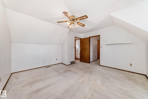 Spacious room featuring sloped ceilings, a ceiling fan with light fixture, light-colored carpet flooring, and dark wood trim - 9528 189 Street, Edmonton, AB - Indoor Photo Showing Other Room
