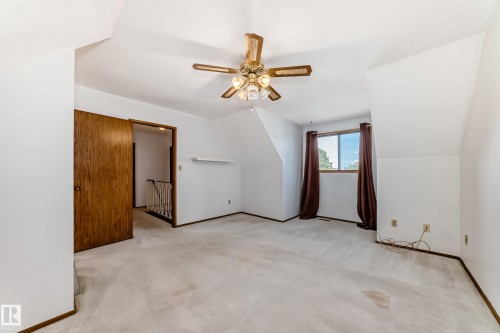 Carpeted room featuring a ceiling fan with integrated lighting, a window with brown drapes, and a wooden door - 9528 189 Street, Edmonton, AB - Indoor Photo Showing Other Room