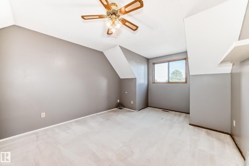 Carpeted room featuring a ceiling fan with integrated lighting, a window with a wood frame, sloped ceiling details, and a built-in wall shelf - 9528 189 Street, Edmonton, AB - Indoor Photo Showing Other Room