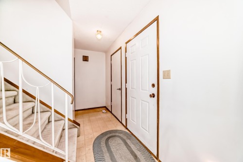 Entryway featuring a paneled door with brass hardware, tile flooring, and a carpeted staircase with a decorative metal railing and wood-finish trim - 9528 189 Street, Edmonton, AB - Indoor Photo Showing Other Room
