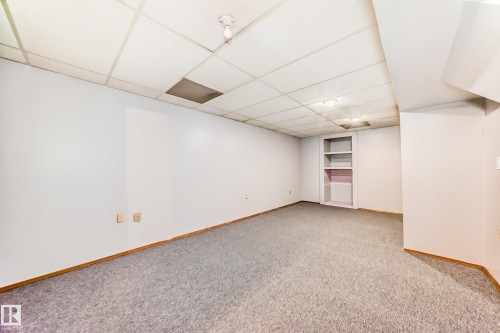 Spacious room featuring light gray carpeting, white walls, wood trim baseboards, a dropped ceiling with square panels, and built-in shelving - 9528 189 Street, Edmonton, AB - Indoor Photo Showing Other Room